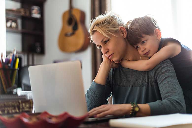 woman being hugged by child while she works at laptop
